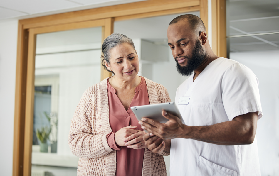 MALE HEALTHCARE PROFESSIONAL SHOWING AN IPAD TO A FEMALE PATIENT